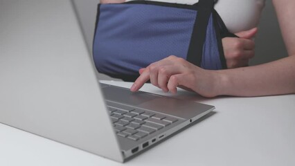 Person with disability, broken arm in sling, working at laptop computer. Woman with trauma lifestyle