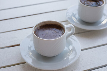 Two white cups of Turkish coffee on saucer on light wooden table. Lifestyle background with copy space.