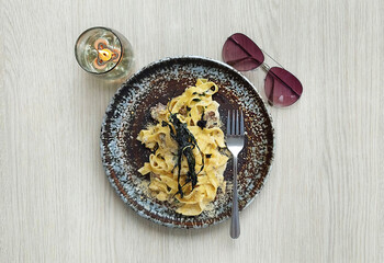 Truffle Cream Mushroom Fettucine on a grungy texture plate served on a white wooden rustic table, with sunglasses for a perfect picnic brunch set.
