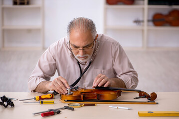 Old male repairman repairing musical instruments at workshop