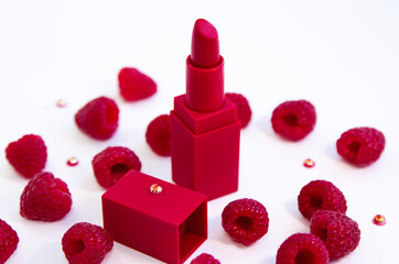 Bright red lipstick and ripe juicy raspberries on white background.