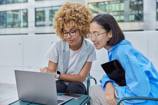 Photo Of Mixed Race Women Talk About Business Innovations And Trade Use Modern Technologies Focused At Laptop Screen Browses Financial Marketing Information Enjoy Brainstorming Collaboration