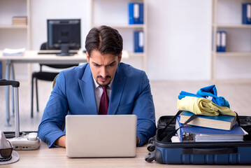 Young male employee preparing for trip at workplace