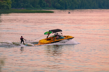 A boat pulls a person over the waves on a wakeboard. Wakeboarding at sunset