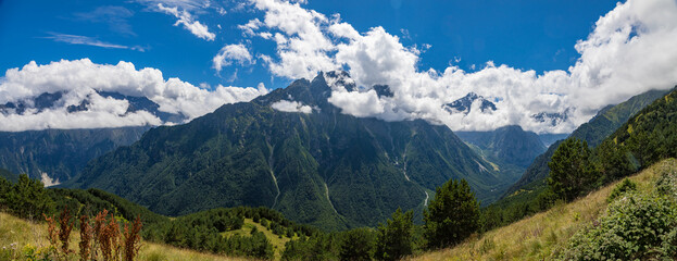 Naklejka na ściany i meble Panorama of mountains with beautiful clouds and waterfalls in North Ossetia.