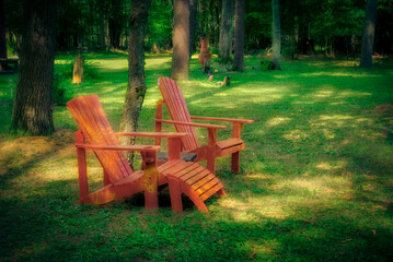 Two Adirondack style chairs, one a lounge, sit in the soft dappled light in a yard in Upstate NY.  Come sit here is what these chairs seem to be saying this Summer Evening.