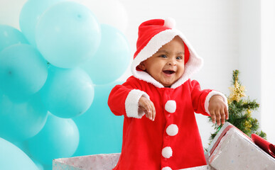 baby girl toddler sitting in a large gift box white background with a Christmas tree, balloons