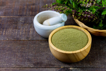 Holy basil powder on wooden bowl with branch and white mortar and pestle on rustic wooden...
