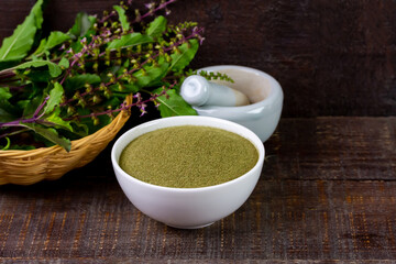 Holy basil powder on white bowl with branch and white mortar and pestle on rustic wooden background. Holy basil leaf are useful herbs and food ingredient has a spicy flavor. 
