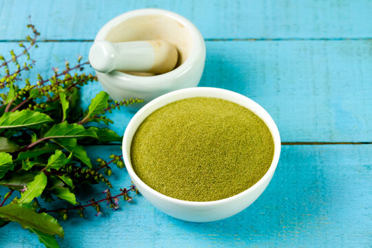 Holy basil powder on white bowl with branch and white mortar and pestle on blue wooden background. Holy basil leaf are useful herbs and food ingredient has a spicy flavor. 