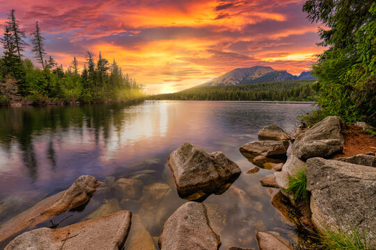 Awesome nature landscape. Beautiful scene with high Tatra mountain peaks, stones in mountain lake, calm lake water, reflection, colorful sunset sky. Amazing nature background. Autumn adventure hiking - Powered by Adobe