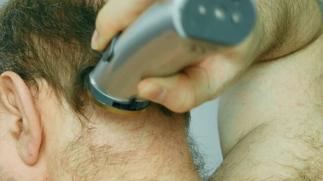 Man shaves his head. An overgrown man with a bald patch clumsily cuts his brown gray hair on his head with an electric clipper. Amateur haircut in the bathroom. Self shaving head with a trimmer