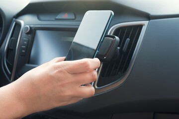Driver attaches the smartphone to a magnetic holder. Close-up of a hand with a phone inside a car. Car accessories. - obrazy, fototapety, plakaty