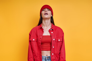 Playful young woman in red hat and looking at camera while standing against colored background