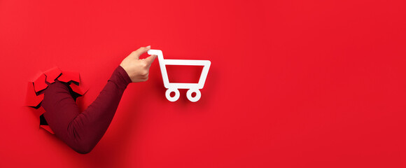shopping cart in hand over red background, panoramic layout