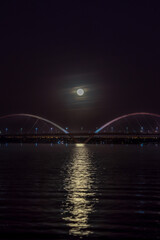 The moon sunset over the JK Bridge in Brasilia, Brazil. Fog over Paranoa Lake. Supermoon rays reflecting in the water.