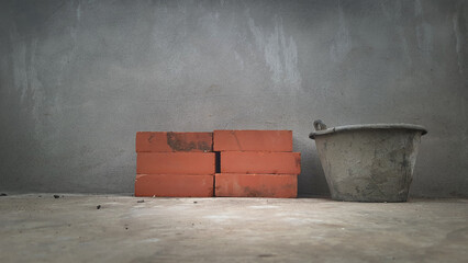 A pile of building materials, bucket mortar mixed and small heap of red bricks at construction site.