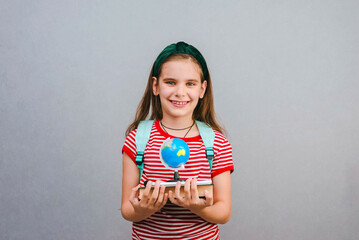 Back to school. Happy child holds a book and globe in her hand on a grey background. Education and...