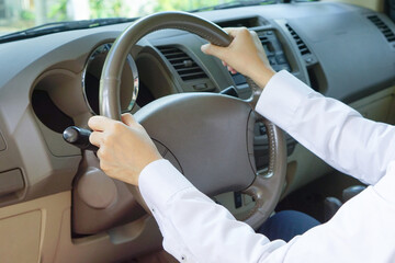 Hand of the man wear white shirt holding on the steering wheel while driving a car.