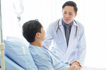 Senior doctor and young male patient who lie on the bed while checking pulse, consult and explain with nurse taking note and supporting in hospital wards.