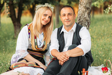 Husband and wife in Serbian traditional clothing, sitting under a tree