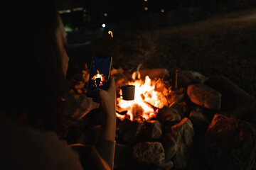 Woman takes a picture of a mug near the campfire. Close up.