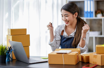 Attractive Asian businesswoman rejoicing as she receives an order from a customer. Young Asian small business owners use computers. Shipping boxes online market SME e-commerce telemarketing concept