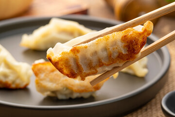 Close up use chopsticks clamp gyoza,Japanese style grilled dumplings with pork and vegetables on black plate
