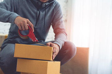 Detail of packing cardboard boxes while moving house. Young man packing box, indoors young male warehouse worker packing boxes for shipment. 