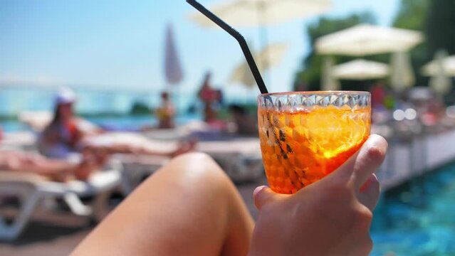 Young woman siting a sun lounger and drink cocktail near swimming pool.Girl enjoy summer vacation by the pool.Sexy woman in bikini having resort relax slow motion.