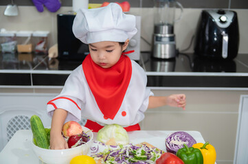 Cute asian girl wear chef uniform with a lot of vegatable on the table in the kitchen room,Make...