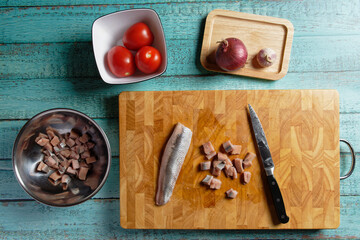 Preparations for a herring salad with pickled herring fillets and tomatoes, on wooden cutting board.