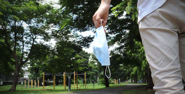 End of coronavirus pandemic. Happy asia guy taking off his protective mask at summer in park