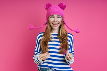 Playful young woman in pink hat smiling while standing against colored background