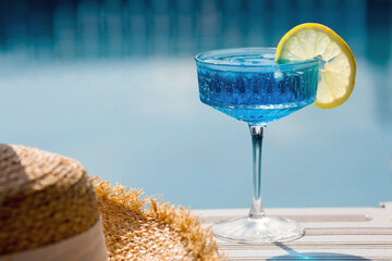 A glass of delicious blue cocktail "Blue Lagoon" and yellow lemons on the background of the pool. Alcoholic cocktail juicy fruit blue with curacao liqueur, ice cubes and a slice of lemon. 