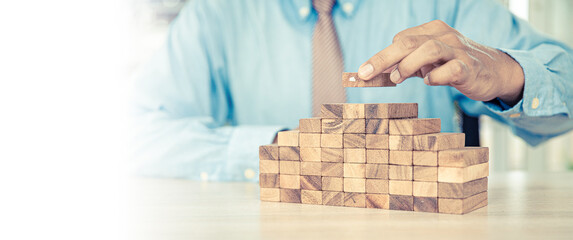Hand placing wooden block tower stack in pyramid stair step with caution to prevent collapse or...