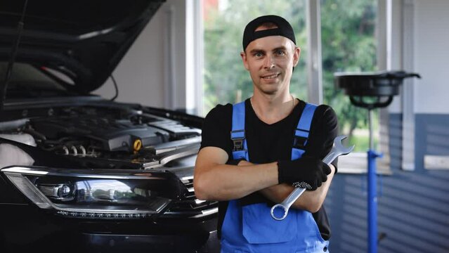 Portrait of european caucasian car mechanic in uniform with tools in his hands looks at the camera and laughs happily. Car service concept
