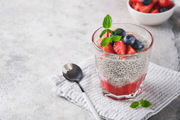 Chia strawberry pudding. Healthy vegan breakfast chia seeds pudding with fresh berries and mint in glass on gray concrete background. Concept of healthy eating, dieting, fitness menu. Selective focus.