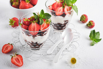 Trifles. Brownies, fresh strawberry and mascarpone cream servered in layers on glass on white background. Portion desserts. No baked brownie cheesecake with fresh berries in a glass.