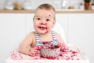 Cute happy baby in high chair with messy face and hands