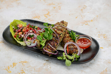 Lyula kebab in a black plate with salad and pomegranate on the table with a glass of wine
