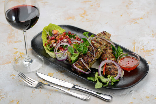 Lyula kebab in a black plate with salad and pomegranate
