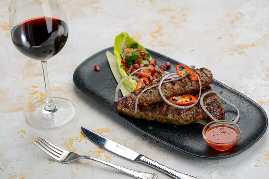 Lyula kebab in a black plate with salad and pomegranate on a white background
