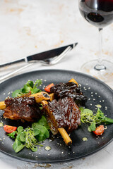 fried ribs in sauce in a black plate on a white background with a glass of wine
