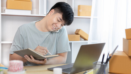 Man selling products online was talking on the phone or chat to receive an order from a customer and list in a notebook, Online shopping SME entrepreneur, Packing box, Sell online, Freelance working.