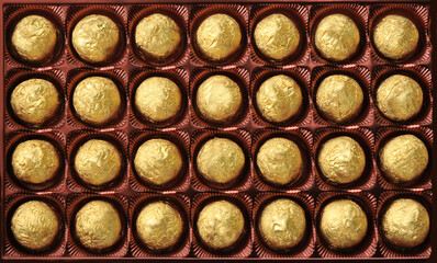  Chocolates wrapped in foil in a box top view, close-up. Background for chocolate and candy products.