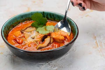 tom yum soup in green plate on white background with spoon in female hands
