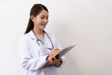 A long-haired brown-haired Asian female doctor in a white medical uniform smiling brightly, is standing with a paper board isolated against the background.