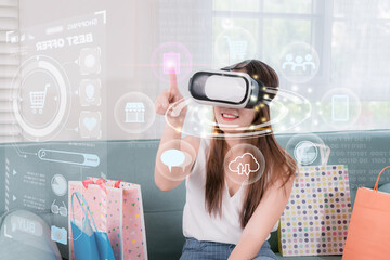 Asian woman touching futuristics icon with shopping bags using virtual reality headset in simulated...