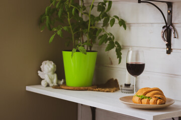 Glass of red wine, sandwich amd home plant on shelf. Lunch concept. Alcohol drink with croissant. Relax time. Lifestyles background. Dinner time. Food and drinks. Home interior. Dinner in patio.